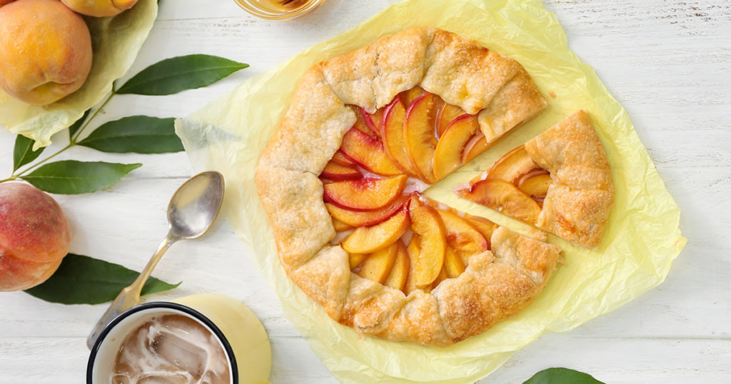 Parchment with delicious peach galette and cup of refreshing drink on white wooden table